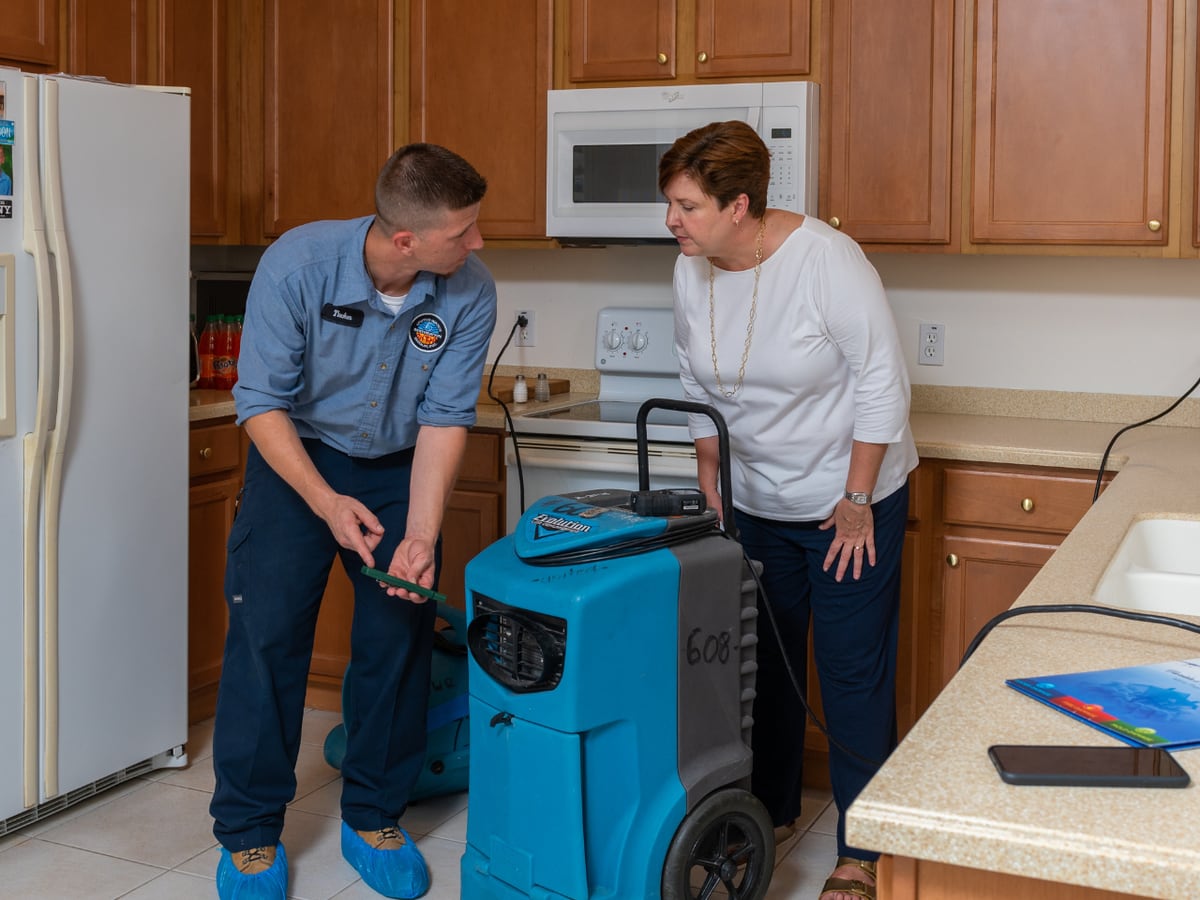 Two technicians setting up drying equipment in a kitchen